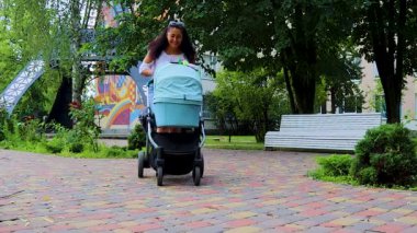 Parkta Yürüyüş yaparken Bebek Arabasında Bebeğiyle Konuşan Mutlu Anne. Mutlu bir annenin portresi, Summer Park 'ta Çocukla Rahatlıyor.