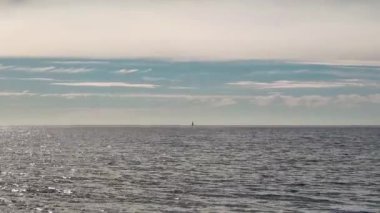 Açık mavi bir gökyüzü ve ufukta bir yelkenli olan sakin bir deniz. Tatilde sakin bir atmosfer.