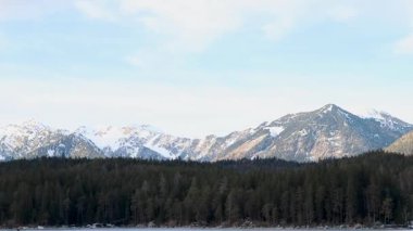 Önplanda karlı tepeler ve dingin göl ile nefes kesici dağ manzarası