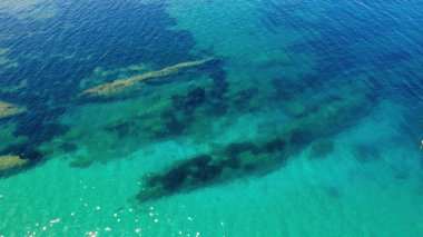 Su altındaki kayaları ve muhtemelen deniz yaşamını açığa çıkaran berrak turkuaz suların çarpıcı görüntüsü. Bu kıyı bölgesi güneşli bir öğleden sonra doğal güzellikleri sergiliyor..