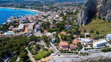 Güneşli bir günde kıyı şeridi boyunca renkli binalar, yemyeşil ve kumlu plajlar olan büyüleyici bir sahil kasabasını gösteren panoramik bir manzara..