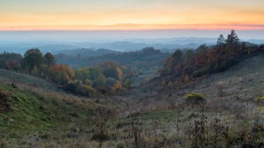 Sonbaharda alacakaranlıkta kırsal alan, yemyeşil ormanları ve gökyüzünde turuncu parıltısıyla dağlık kırsal bölge.