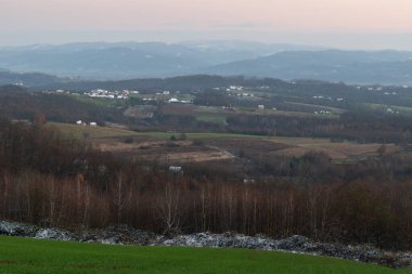 Peaceful hilly village panorama at dusk, first snow on house rooftops, lovely evening in countryside