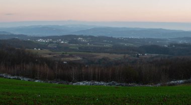 Peaceful hilly village panorama at dusk, first snow on house rooftops, lovely evening in countryside