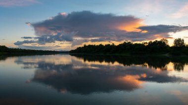Su yüzeyinde büyük kümülonimbus bulutu simetrik yansıması, dramatik ışık ile toz bulutu ve nehir manzarası