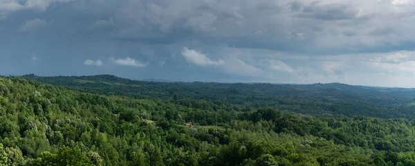 Dark clouds above hilly scattered village, stormy cloud and countryside overgrown with forest