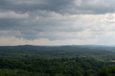 Tepedeki kara bulutlar yağmur üstüne güneş lekeleri, yemyeşil orman ve dağınık evler.