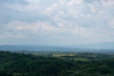 Güneş lekesi, tepe tabakalarına karşı sisli tepe manzarası, yemyeşil ormanlar ve yaz mevsiminde dağılmış bir köy. Gökyüzünde büyük bulutlar var.