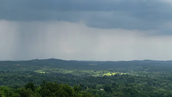 Cloudburst over hilly countryside and sun spots on forest and scattered village