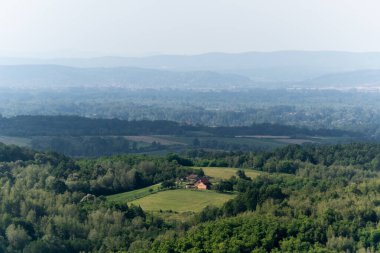 Kırsal ev, yemyeşil ormanlarla çevrili, tepe katmanları puslu.