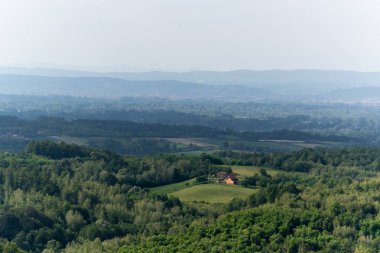 Kırsal ev, yemyeşil ormanlarla çevrili, tepe katmanları puslu.