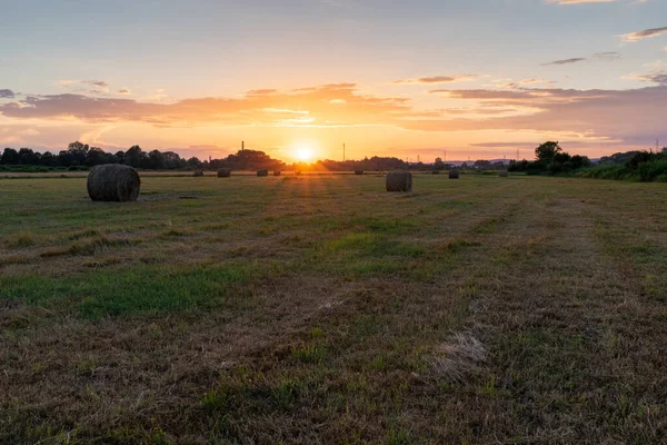 stock image Round hay bales on field at golden sunset, sunset in countryside with bright colorful clouds