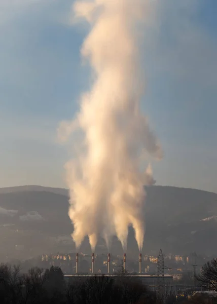 Huge cloud of smoke or steam rises above chimney of heating plant, city heating plant in Banja Luka and Ponir hill in background