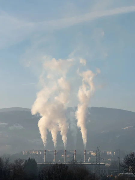 Huge cloud of smoke or steam rises above chimney of heating plant, city heating plant in Banja Luka and Ponir hill in background