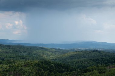 Yaz mevsiminde ağaçların arasında, dağların tepelerinde sağanak yağış görülür.