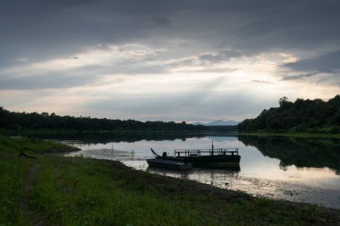 Nehirde demirli teknelerin bulunduğu manzara dağ siluetine karşı uzaklık ve bulutlardan gelen güneş ışınları