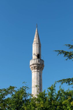Mavi gökyüzüne karşı cami minaresi, ağaç tepe örtüsünün üstünde