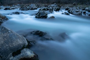 Mavi saatte, ipeksi suyla birlikte dağ deresi, ıslak kayaların etrafında uzun süre akan dere.