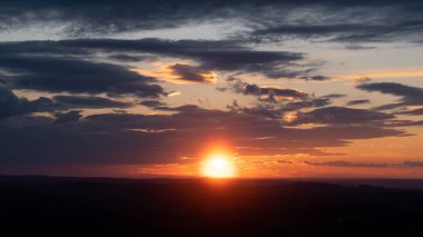 Parlak güneş gökyüzünde bulutlarla kırsal alanda batıyor.