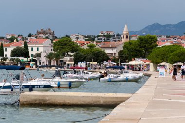 Novalja 'da turistlerle rıhtım, denizde demirli tekneler.