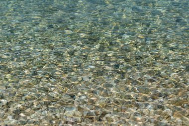 Dalgalanan deniz suyu yüzeyi, dipte temiz sığ su ve taşlar.
