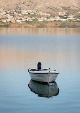 Tekne denize demirlemiş, karada evleri uzakta.