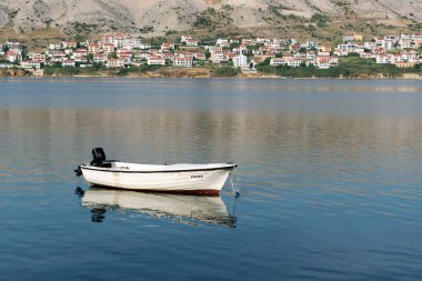 Tekne denize demirlemiş, karada evleri uzakta.