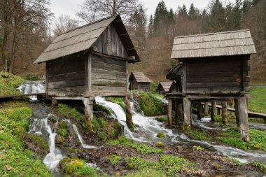 Hava bulutluyken Jajce yakınlarındaki Pliva nehrinde küçük tahta su değirmenleri