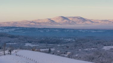 Şafak vakti, güneş ışığında uzak dağlarla Hilly köyü, kışın manzarası