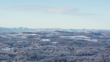 Soğuk kış gecesinden sonra buzla kaplı tepe köyü, yaprak döken orman ve tarlalarla kaplı manzara, dağ sıraları