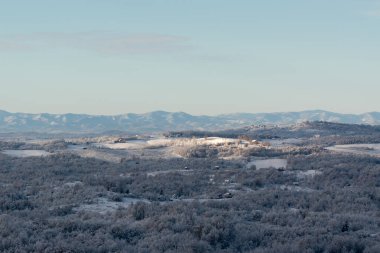 Soğuk kış gecesinden sonra buzla kaplı tepe köyü, evlerle, yaprak döken ormanlarla ve tarlalarla dolu kırsal arazi, dağ sıraları.