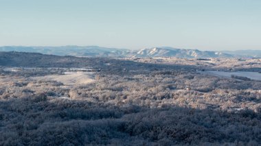 Soğuk kış gecesinden sonra buzla kaplı tepe köyü, evlerle, yaprak döken ormanlarla ve tarlalarla dolu kırsal arazi, dağ sıraları.