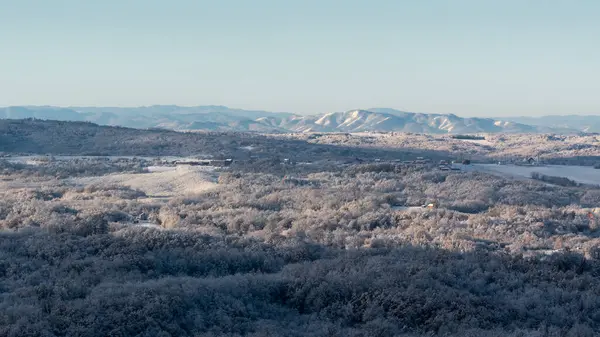 Soğuk kış gecesinden sonra buzla kaplı tepe köyü, evlerle, yaprak döken ormanlarla ve tarlalarla dolu kırsal arazi, dağ sıraları.