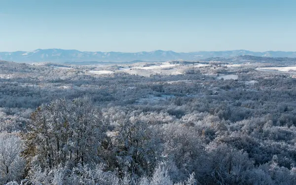 Soğuk kış gecesinden sonra buzla kaplı tepe köyü, evlerle, yaprak döken ormanlarla ve tarlalarla dolu kırsal arazi, dağ sıraları.