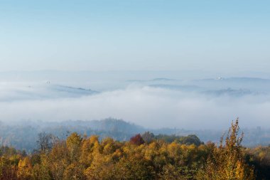 Tepelerden vadiye doğru sis yağıyor, tepede kilise, sonbahar manzarası var.