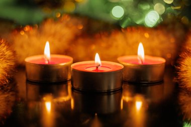 Köknar dalları ve kırmızı böğürtlenli üç parlak Noel mumu karanlıkta yanıyor. Mumların arkasında bulanık bir Noel resmi küçük bir ev hediye ve çelenktir. Yeni yıl arifesi. Maytaplar.