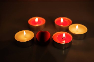 Mumlar karanlıkta yanıyorlar. Kırmızı mumlar siyah arka planda kalp şeklinde dizilir. Gül yaprakları mumların etrafına saçılmış. Metin için yeri olan pankart.