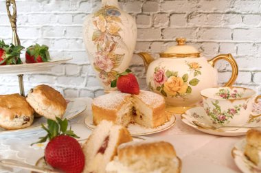 Geleneksel öğleden sonra çayı Vintage tarzı kremalı çörekler çilek ve kremalı geleneksel Victoria usulü sünger klasik porselen tabaklar ve çay fincanları. 