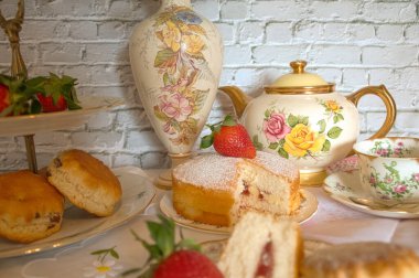Geleneksel öğleden sonra çayı Vintage tarzı kremalı çörekler çilek ve kremalı geleneksel Victoria usulü sünger klasik porselen tabaklar ve çay fincanları. 