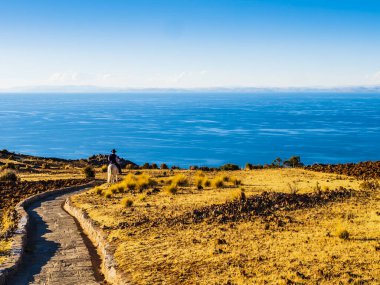 Stunning view of lake Titicaca at sunset, with a local farmer riding down to the village through a stone path, Amantani island, Peru 