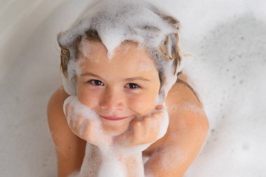 Çocuk şampuanı. Şampuan köpüğü ve banyo yapan saçlarında kabarcıklar olan bir çocuk. Köpüklü çocuk suratı, saç bakımı ve hijyen konsepti. Çocuklar uzun saçlar için şampuan kullanırlar. Banyoda saç yıkamak.