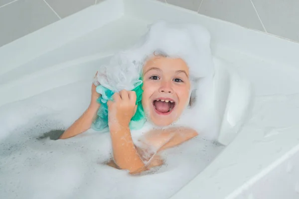 Children bathing. Kid in a bath tub. Washing in bath with soap suds on hair. Child taking bath. Closeup portrait of smiling kid, health care and kids hygiene. Kids face in bath tub with foam