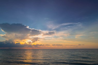 Gökyüzü ve bulutların arasından güneş batarken deniz batıyor. Okyanus ve gökyüzü arkaplanı, deniz manzarası.