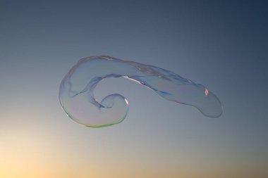 Mavi gökyüzünde uçan büyük bir baloncuk. Bulutlu arka planda kocaman renkli sabun köpükleri uçuşuyor.