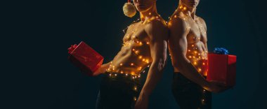 Elinde hediye tutan kaslı genç bir adam. Noel zamanı. Seksi kaslı erkekler. İkiz kavramı. Çıplak vücutlu iki ikiz kardeş.