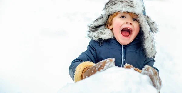Winter banner. Excited child playing with snow in park on white snow background. Funny child in winter hat make snow ball in winter park outdoor. Winter games with snow for kids