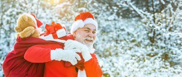 サンタの雪のシーンに対する贈り物の袋を運ぶ 冬のクリスマスグリーティングカード サンタクロースは白い自然の背景に贈り物の巨大な袋を引く — ストック写真