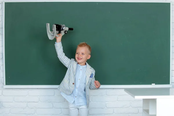 学校の子供だ 子供は黒板を背景に授業で学んでいる 早期教育 顕微鏡を持った小さな子供 — ストック写真