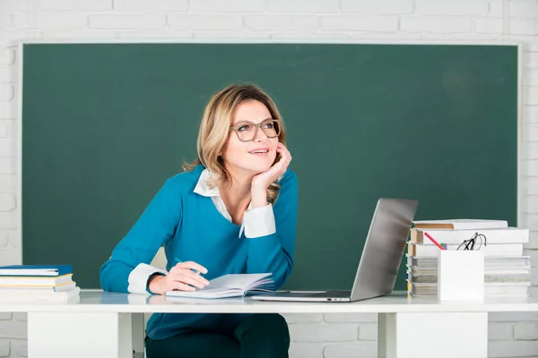 Female teacher. Portrait of female teacher teaching line of high school students with notebook in classroom on blackboard