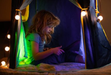 Çocuk yatakta yatıyor ve sanal online okul dersinde öğreniyor. Çocuk evde dizüstü bilgisayarla çalışıyor. Dizüstü bilgisayar kullanan bir çocuk. Çocuklar için evde eğitim